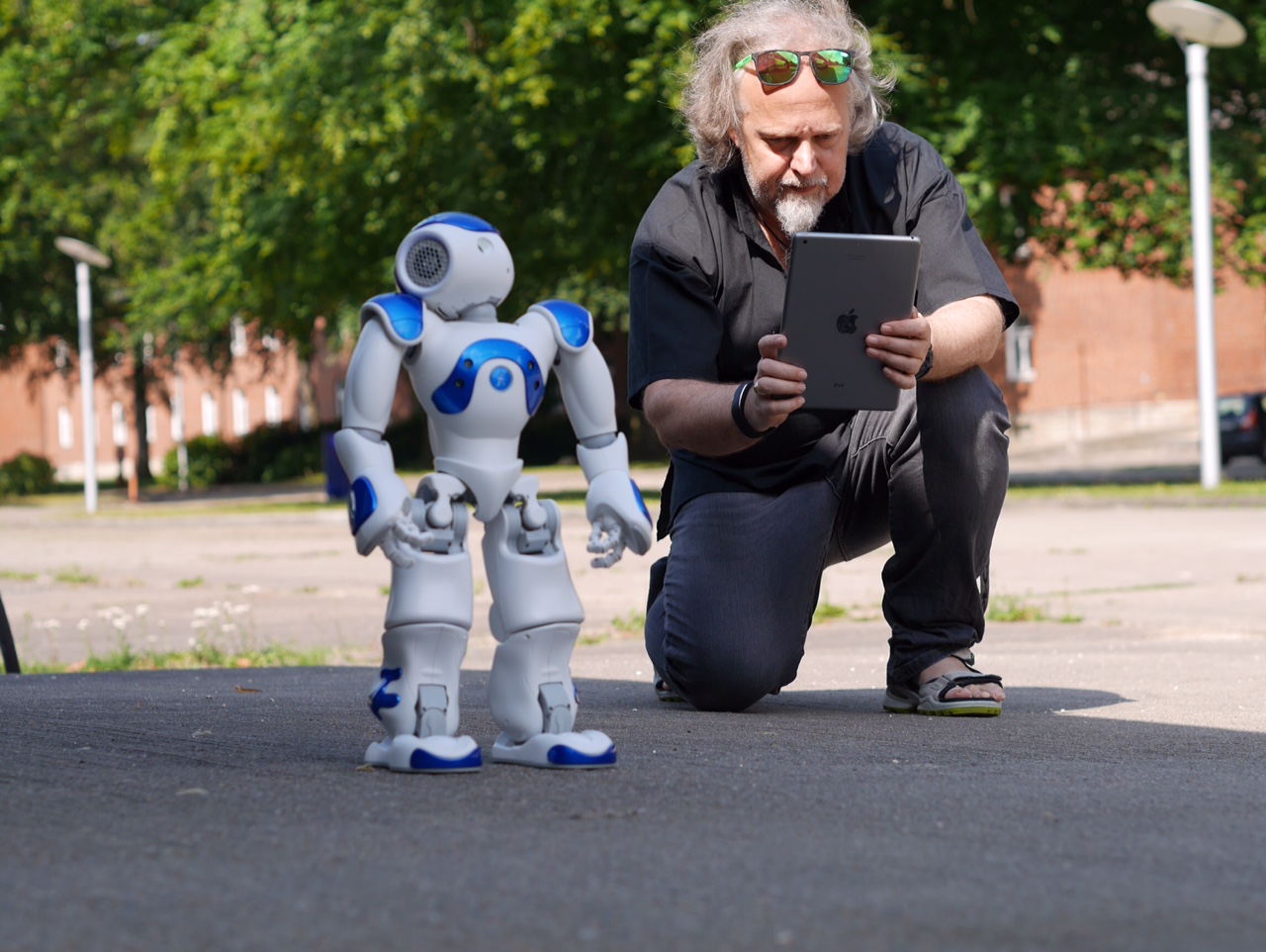 Ein Mann kniet mit einem Tablet neben einem knapp einen Meter großen Roboter.