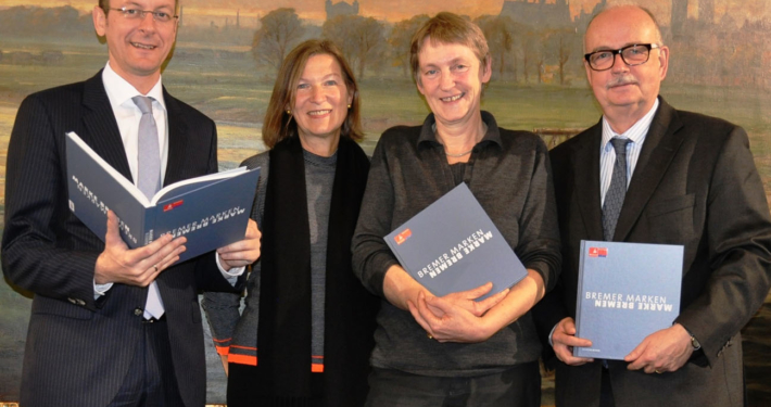 Zwei Frauen und zwei Männer posieren für das Bild, drei von ihnen halten Bücher in der Hand.