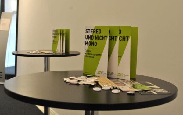 Auf einem runden Tisch stehen Flyer mit dem Titel: Stereo und nicht Mono.
