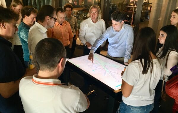 Mehrere Personen stehen um einen nach oben zeigenden großen Bildschirm herum und schauen auf ihn.