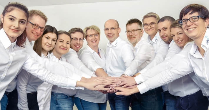 Eine Gruppe Menschen in weißen Hemden posiert im Halbkreis für das Bild, dabei halten alle eine Hand in die Mitte.