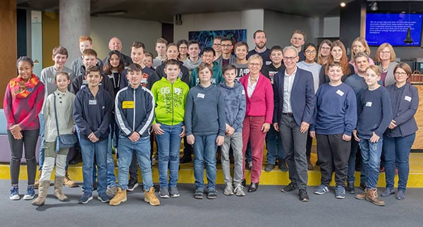 Eine Gruppe Schülerinnen und Schüler steht mit zwei Erwachsenen draußen für ein Gruppenfoto zusammen.