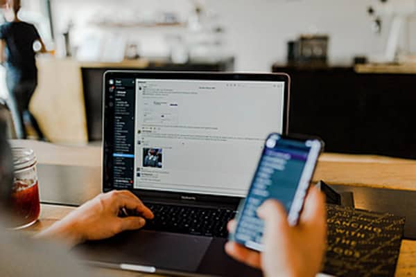 Eine Person sitzt vor einem Computer und hat gleichzeitig ein Handy in der Hand.