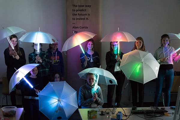 Ein Gruppe Mädchen hält bunt leuchtende Regenschirme über ihre Köpfe.