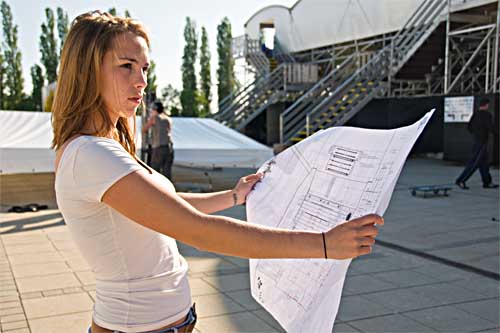 Eine Frau steht draußen vor einem Gebäude und hält einen ausgebreiteten Faltplan in den Händen.