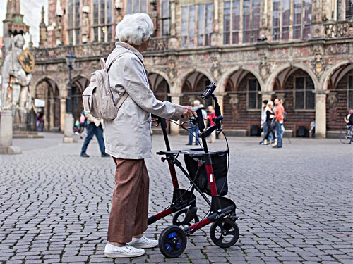 Eine ältere Dame steht mit einer Gehhilfe auf dem Bremer Marktplatz und schaut auf das Rathaus.
