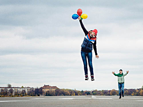 Eine Person mit Luftballoons in der Hand schwebt über dem Boden, im Hintergund läuft eine Person mit ausgestreckten Armen.