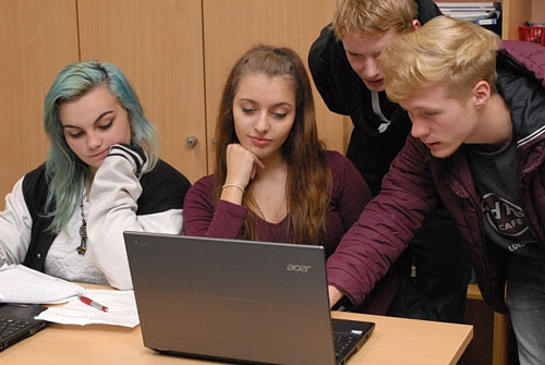Zwei Mädchen und zwei Jungen vor einem Laptop, ein Junge hat die Hand auf der Tastatur.