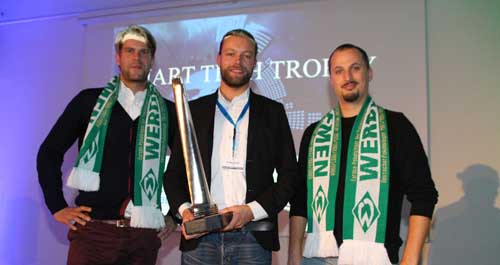 Drei Männer posieren für das Bild, zwei von ihnen tragen grün-weiße Schals von Werder Bremen.