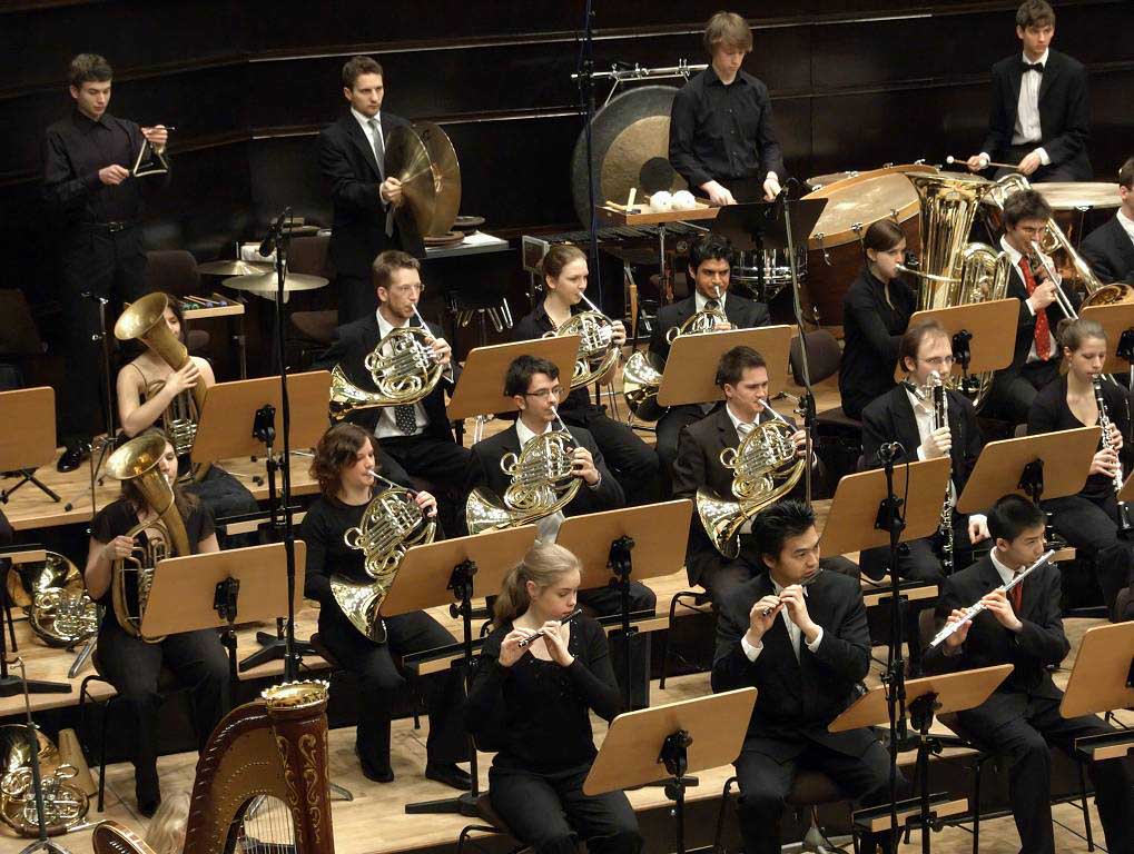 Junge Menschen sitzen in einem Orchester zusammen und spielen verschiedene Blasinstrumente.