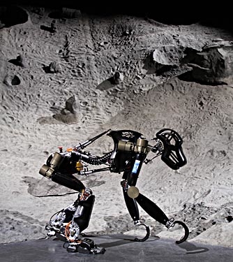 Ein Roboter, dessen Form sich an der eines Affen orientiert, steht vor einer künstlichen Mondlandschaft.