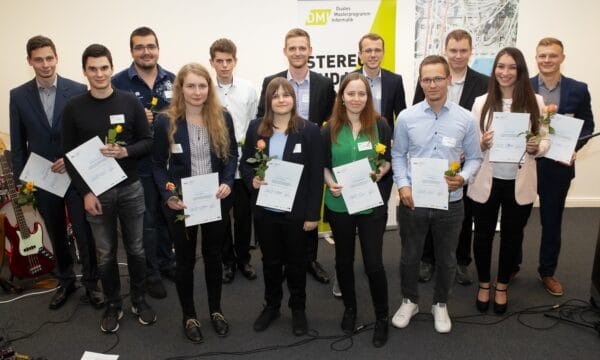 Ein Gruppenfoto von 13 Personen, die jeweils eine Urkunde und eine Rose in der Hand halten und in die Kamera schauen.