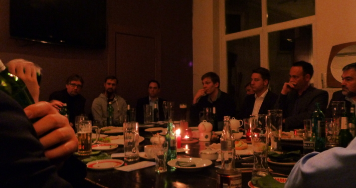 In einem abgedunkelten Raum/Restaurant sitzt eine Gruppe Menschen um einen Tisch.