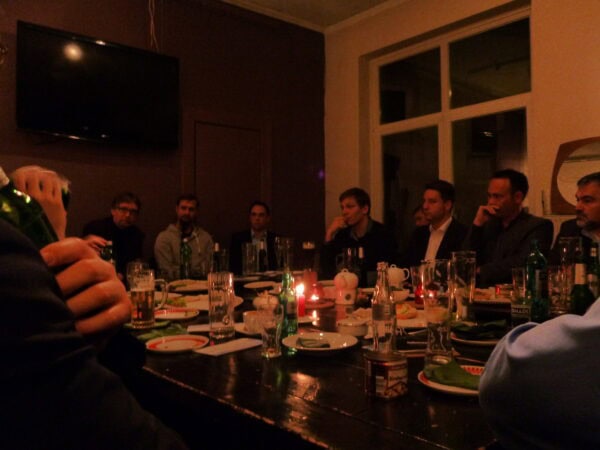 In einem abgedunkelten Raum/Restaurant sitzt eine Gruppe Menschen um einen Tisch.