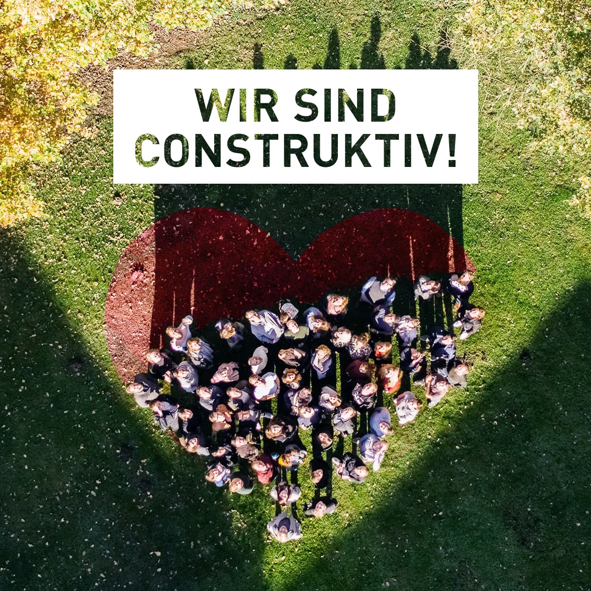 Eine Gruppe Menschen steht auf einer Wiese und formt ein Herz, darüber steht der Satz Wir sind construktiv.