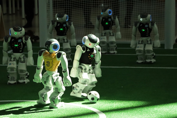 Zwei Roboter spielen auf Kunstrasen Fußball.