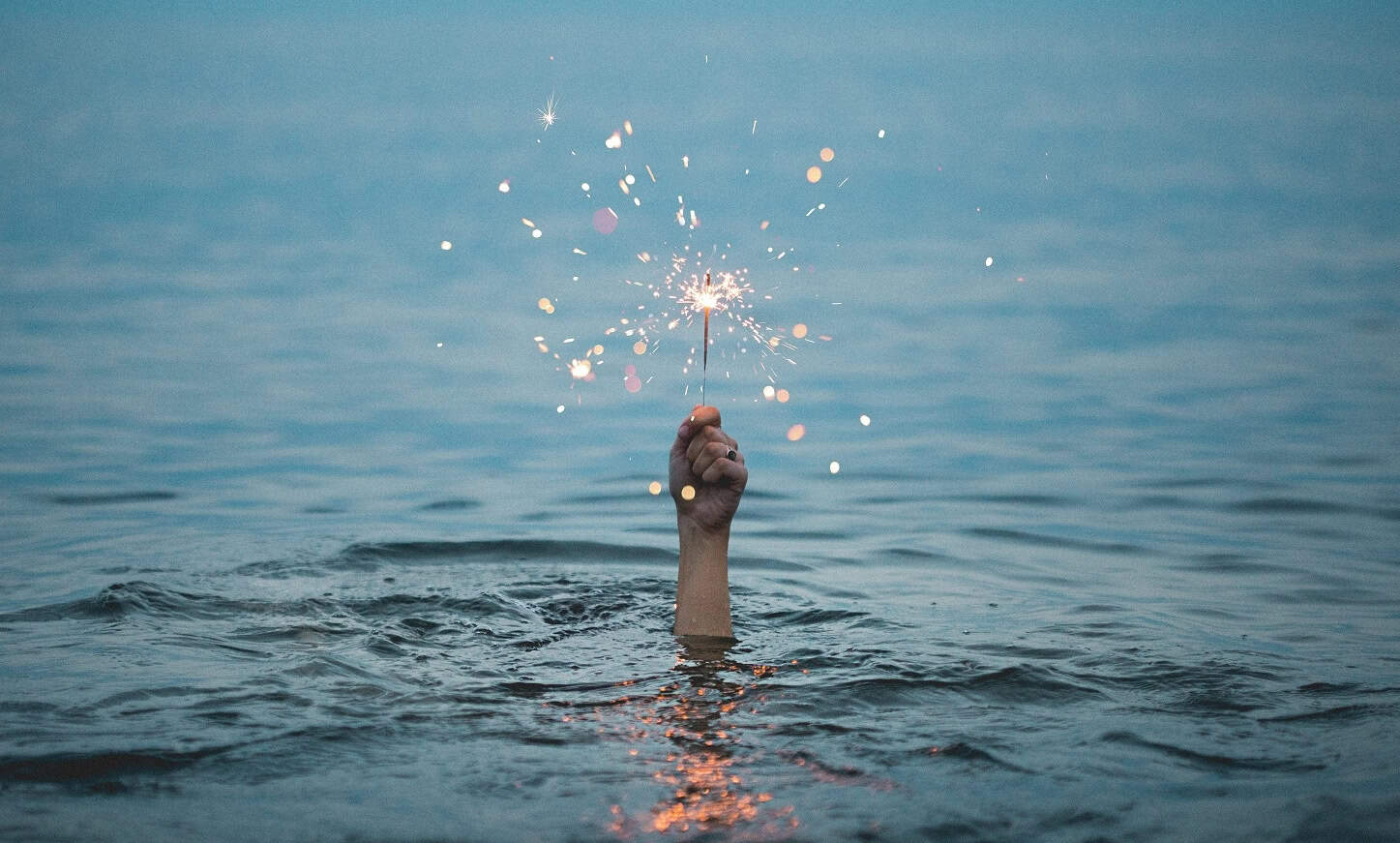 Eine Hand ragt aus dem Wasser und hält eine angezündete Wunderkerze.