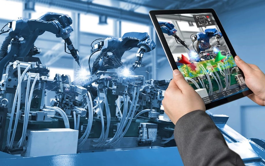 Zwei Hände halten ein Tablet, das auf einen arbeitenden Roboter gerichtet ist.
