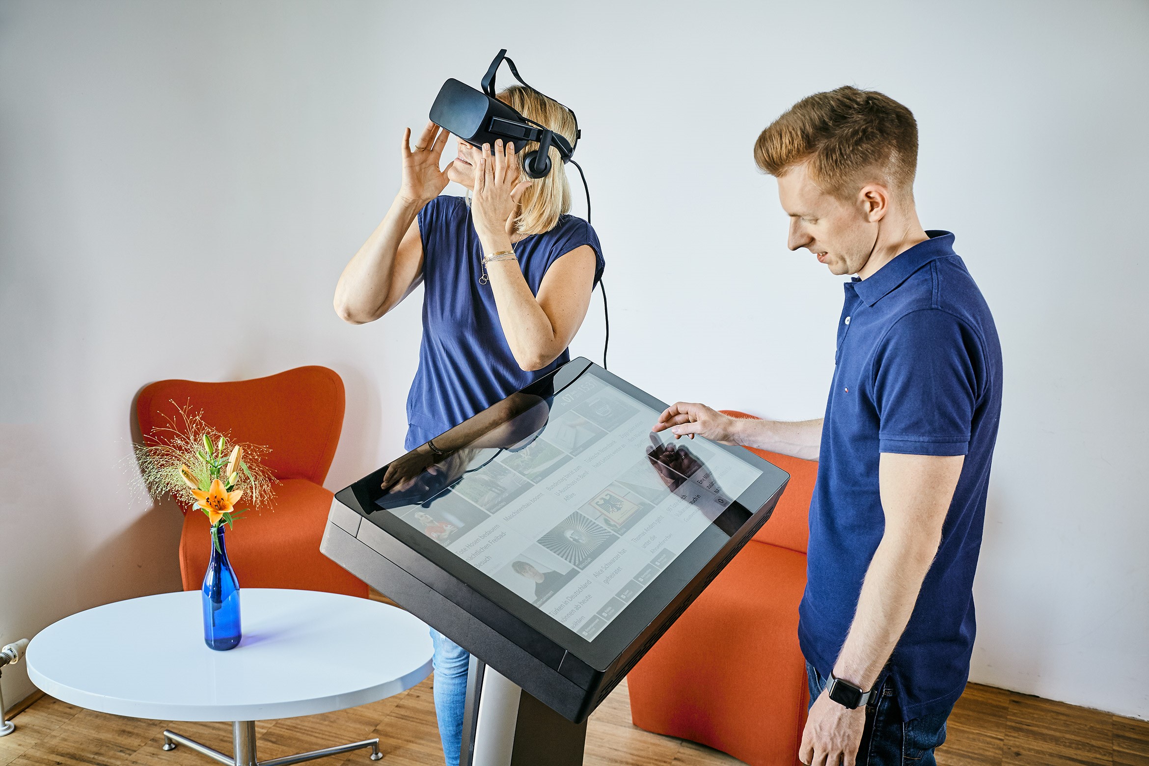 Ein Mann steht an einem großen Touchscreen, neben ihm steht eine Frau mit einer VR-Brille.