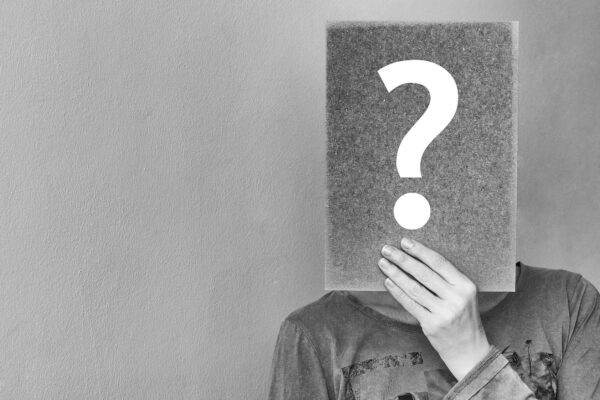 Foto mit Frau die Papier mit Fragezeichen vor dem Gesicht hochhält.