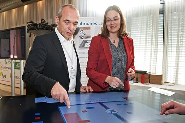 Ein Mann und eine Frau stehen an einem Tisch mit Touchscreen
