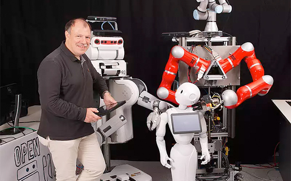 Professor Michael Beetz steht inmitten verschiedener Roboter