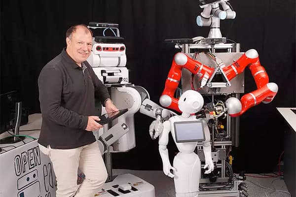 Professor Michael Beetz steht inmitten verschiedener Roboter