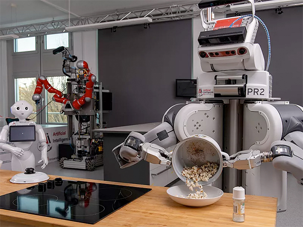 Ein Roboter steht in einer Labor-Küche und schüttet Popcorn in einen Teller.