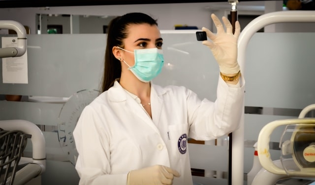 EIne Frau mit Kittel, Mundschutz und Handschuhen hält eine Laborprobe in der Hand.