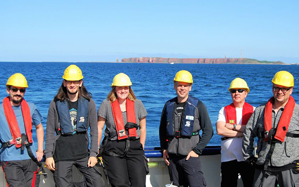 Gruppenfoto mit Personen mit Schutzhelmen und Schwimmwesten auf einem Boot