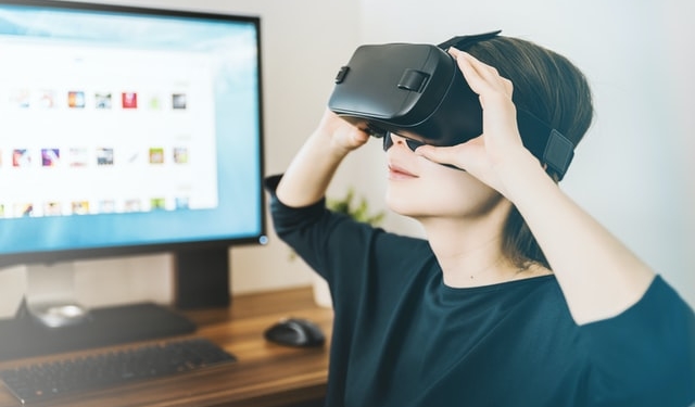 Eine Person trägt eine VR-Brille, im Hintergrund steht ein Computer.