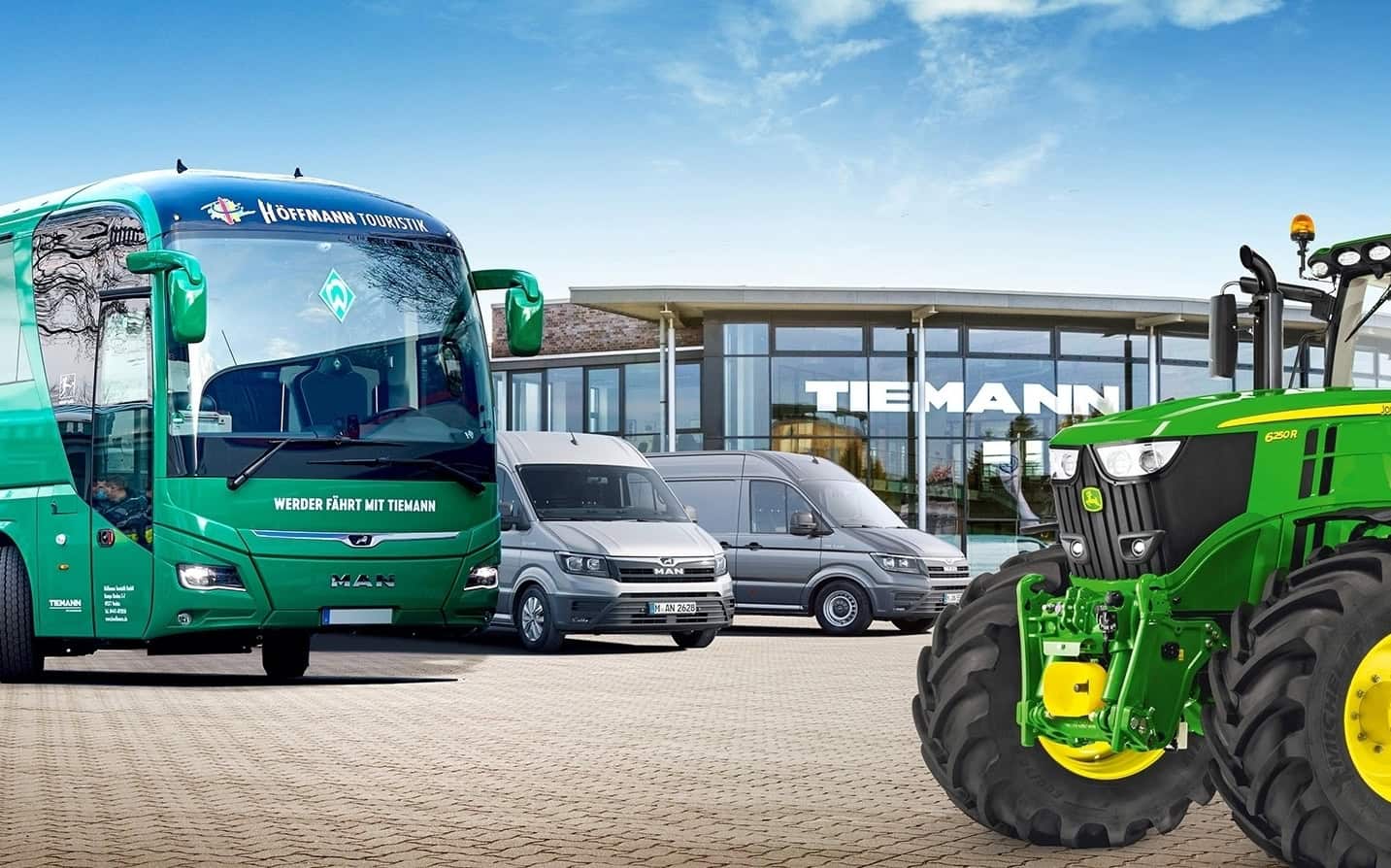 Ein Furpark an großen Fahrzeugen: Ein Bus, ein Trakor und zwei Sprinter, im Hintergrund ein Gebäude mit Glasfront, darauf der Schriftzug Tiemann.