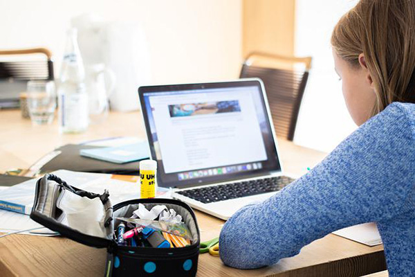 Eine junge Person sitzt mit dem seitlichen Rücken zum Bild vor einem Laptop am Schreibtisch.