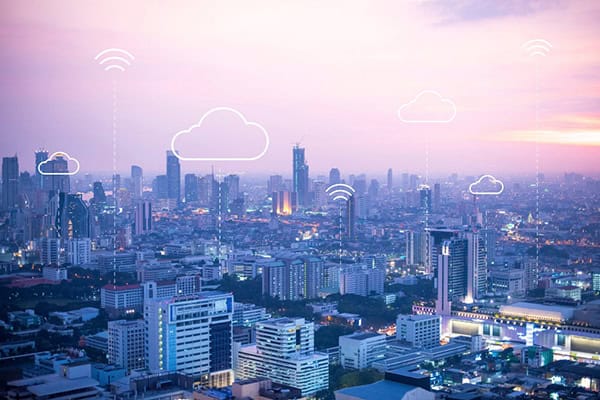 Blick auf die Skyline einer Stadt vor rosa-lilafarbenem Himmel. Darüber liegen Icons von Wolken und dem WLAN-Symbol.