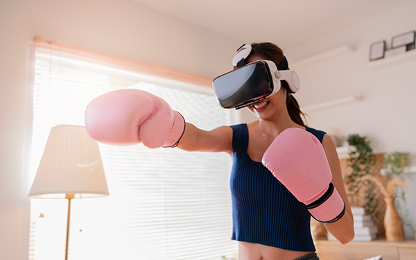Eine Frau steht mit einer VR-Brille vorm Gesicht und in Boxhandschuhen im Wohnzimer und ist in einer Boxbewegung.
