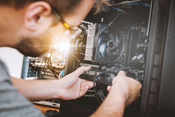 Nahaufnahme einer Person, die ein Hardwareteil an einem größeren Rechner in der Hand hält.