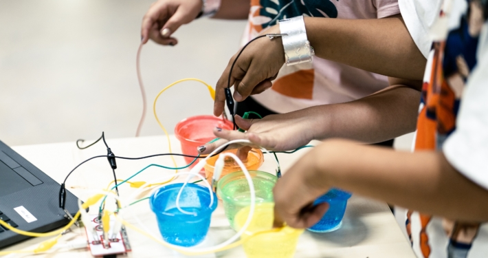 Kinderhände bauen ein "Klavier" aus Plastikbechern und Kabeln, die an einen Laptop angeschlossen sind.