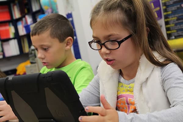 Nahaufnahme zweier Kinder, die an einem Tisch sitzen und auf ein Tablet gucken.