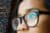 Seitliche Nahaufnahmen eines weiblichen Gesichts mit Brille. Auf den Brillengläsern spiegelt sich Computer-Code.