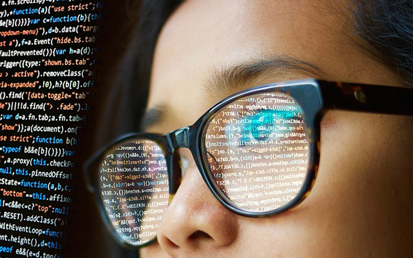 Seitliche Nahaufnahmen eines weiblichen Gesichts mit Brille. Auf den Brillengläsern spiegelt sich Computer-Code.