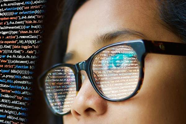 Seitliche Nahaufnahmen eines weiblichen Gesichts mit Brille. Auf den Brillengläsern spiegelt sich Computer-Code.