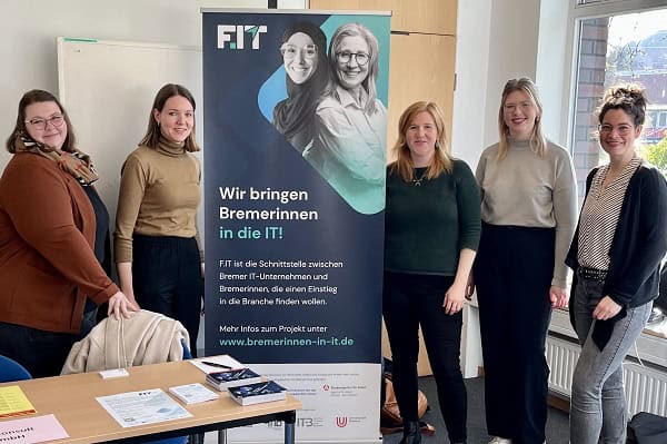 Fünf Frauen stehen um ein Rollup und lächeln in die Kamera.