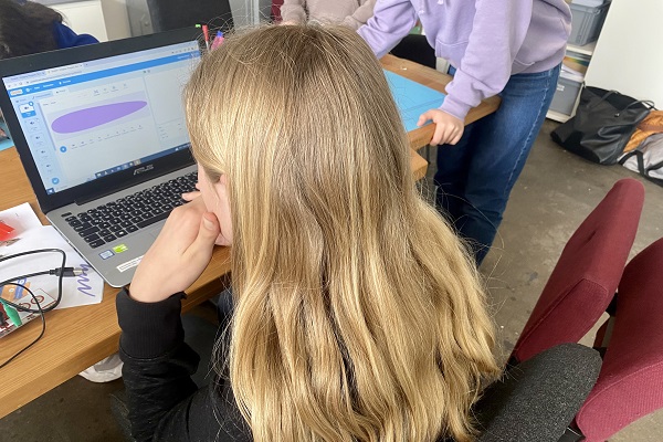 Schulterblick auf ein Mädchen, dass vor einem Laptop sitzt.