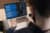 Nahaufnahmen eines aufgekapllten Laptops. Davor sieht man verschwommen die Umrisse eines Kopfes und zweier Arme, die Hände ruhen auf dem Laptop.