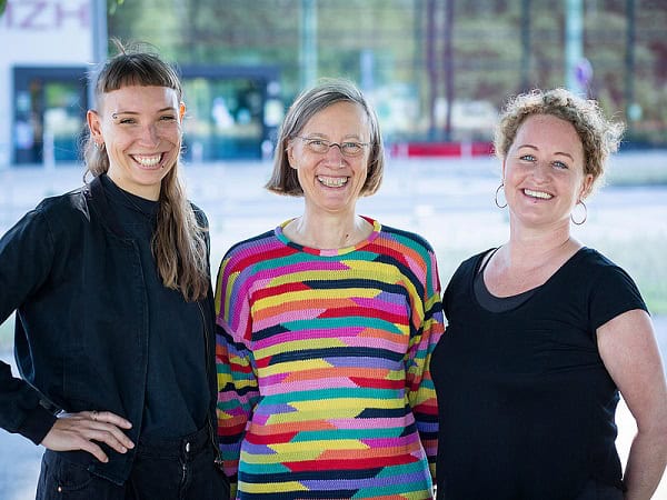 Drei Frauen posieren für ein Foto und lachen in die Kamera.