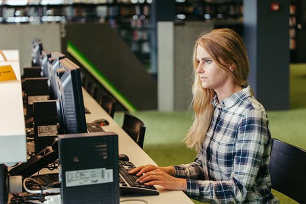 Seitliche Sicht auf eine Frau, die an einem Schreibtisch sitzt und an einem PC tippt.