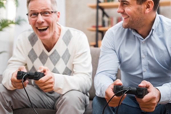Zwei Männer sitzen mit Games-Controllern auf dem Sofa und scheinen erfreut.