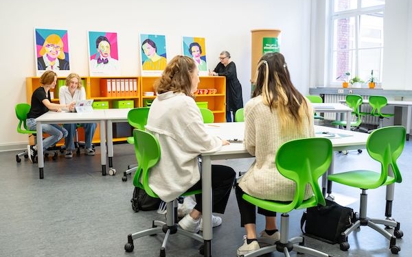 Schüler*innen sitzen in einem Klassenraum auf hellgrünen Stühlen.