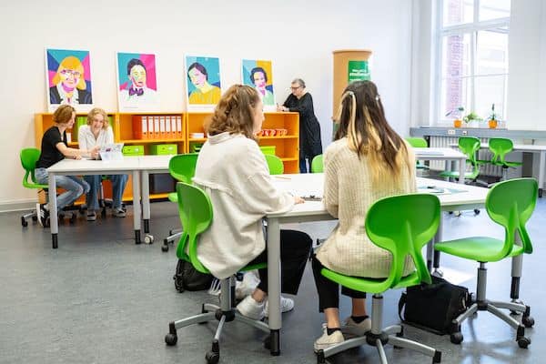 Schüler*innen sitzen in einem Klassenraum auf hellgrünen Stühlen.