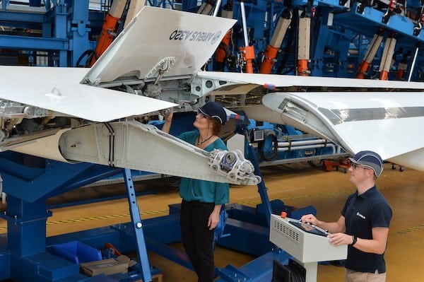 Zwei Menschen arbeiten an einem Flügen eines Flugzeug und tragen einen Schutzhelm.